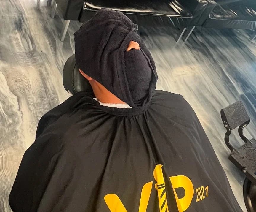 Client reclined under a hot towel in a VIP Barber Lounge cape
